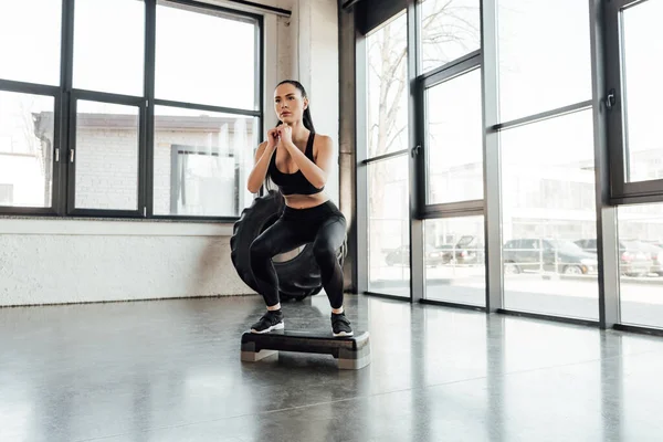 Sportswoman doing squat on step platform in sports center — Stock Photo