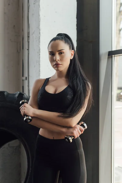 Sexy sportswoman holding dumbbells and looking at camera in gym — Stock Photo