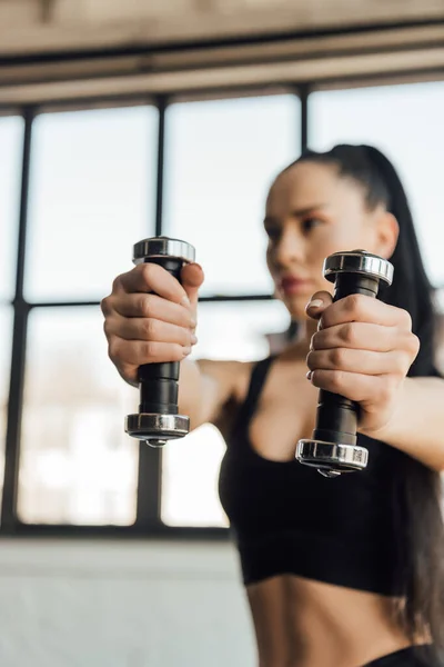 Selective focus of sportswoman holding dumbbells with outstretched hands in gym — Stock Photo