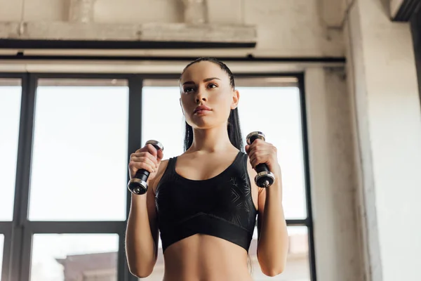 Attractive sportswoman in sports top holding dumbbells in gym — Stock Photo