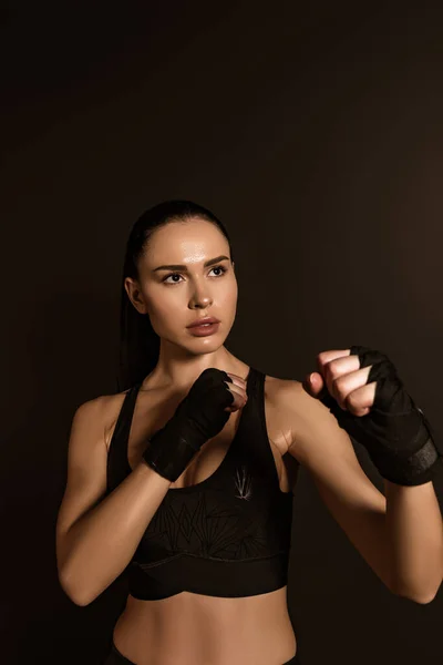 Sportswoman in sports gloves standing in fighting position isolated on black — Stock Photo