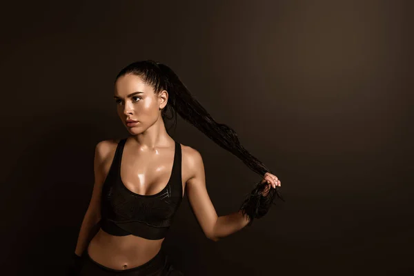 Sexy bruna sportiva toccando i capelli e guardando lontano isolato sul nero — Foto stock