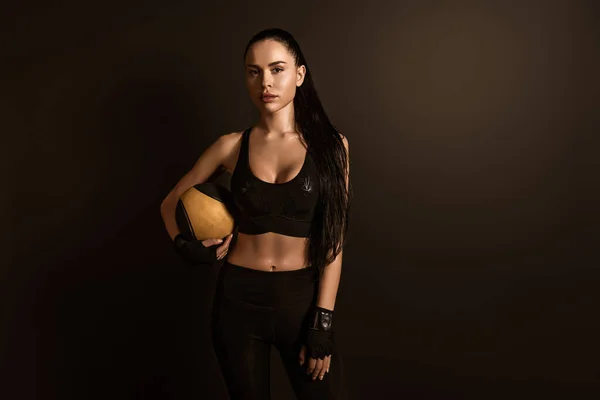 Brunette sportswoman with ball looking at camera isolated on black — Stock Photo