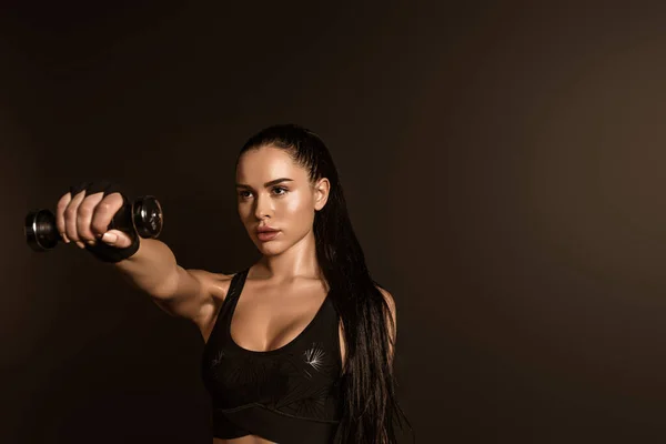 Brunette sportswoman holding dumbbell with outstretched hand isolated on black — Stock Photo