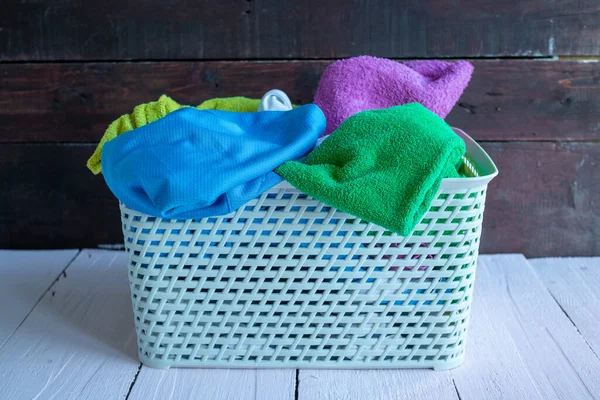 Basket with dirty Laundry on a white wooden background. House cleaning. Dirty Laundry falls out of the basket.