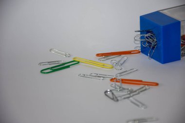 Beyaz arkaplanda mavi kağıt tutacağında birkaç metal ataç.