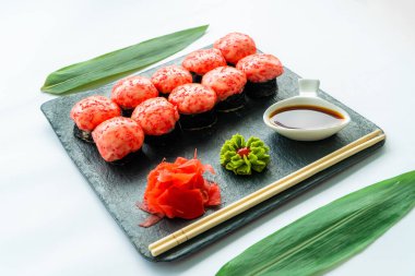 Siyah tabakta kırmızı suşi ve wasabi, zencefil, soya sosu ve çubuklu beyaz arka plan.