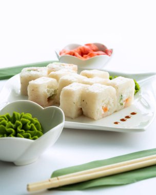 Beyaz bir tabakta beyaz suşi ve wasabi, zencefil ve çubuklu beyaz arka plan.