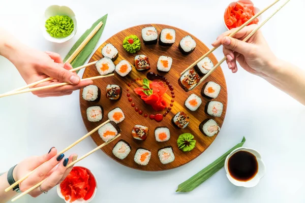 Womans hands hold sushi with chopsticks above the round wooden surface