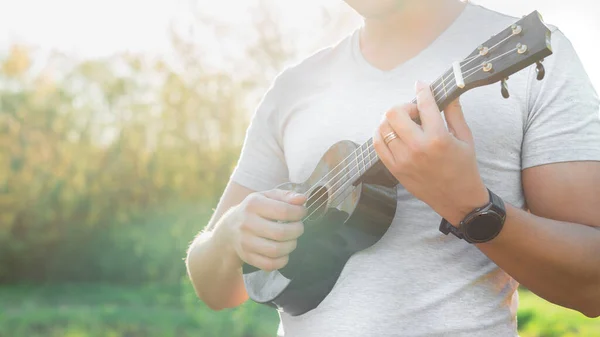 Genç adam parkta ukulele oynuyor. Kapat.
