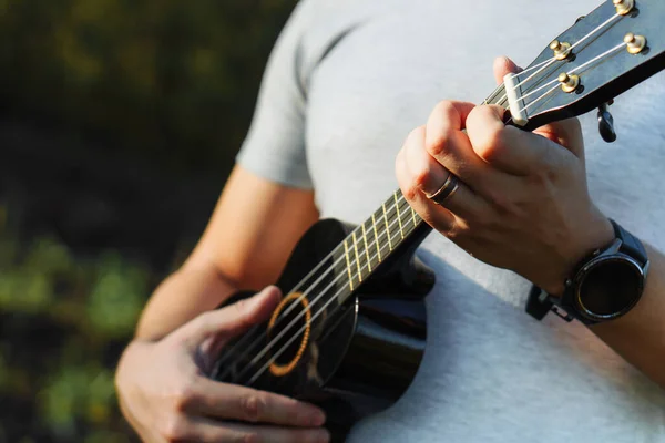 Genç adam parkta ukulele oynuyor. Kapat.
