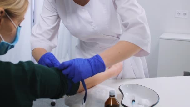 Kvinnlig läkare drar åt bältet på kvinnans hand, desinficerar injektionsstället och tar blod från venen. Efter injektionen klämmer patienten fast en bomullstuss i handen. — Stockvideo