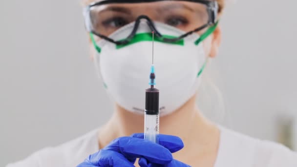 Una doctora está exprimiendo lentamente la sangre de una jeringa. Mujer con máscara protectora, gafas y guantes. Marco de primer plano. Concepto de epidemia y neumonía — Vídeos de Stock