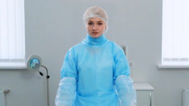 Bir kadın doktor bir hastane odasında kameraya bakıyor. Koruyucu giysili ve şapkalı kadın doktor, koronavirüsü olan hastaların muayenesi için hazırlanıyor. Kamera yavaşça yaklaşıyor.