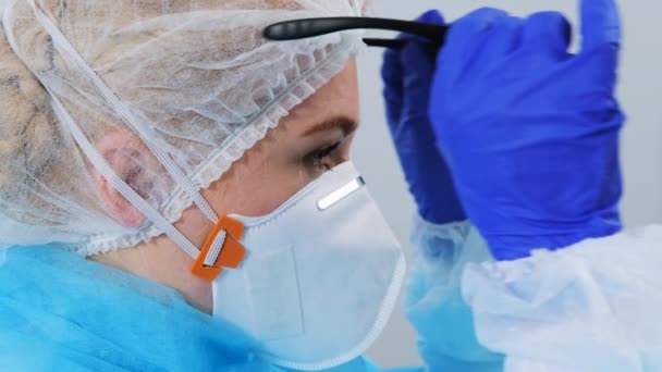 Vista lateral de cerca del trabajador médico se pone gafas de seguridad. Mujer con uniforme protector, respirador y guantes. Fondo blanco, copyspace — Vídeo de stock