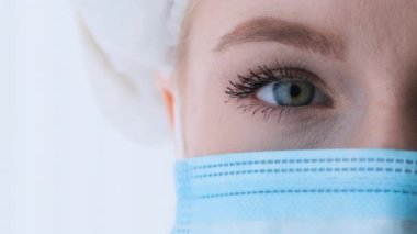 Koruyucu maskeli ve beyaz şapkalı kadın cerrahın yanına. Doktorun gözü.