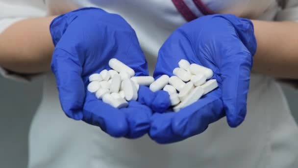 Jovens mulheres doutor em casaco médico branco e luvas azuis de borracha detém um monte de comprimidos comprimidos brancos na palma das mãos. Conceito de Saúde, Drogas, Contracepção, Escolha — Vídeo de Stock