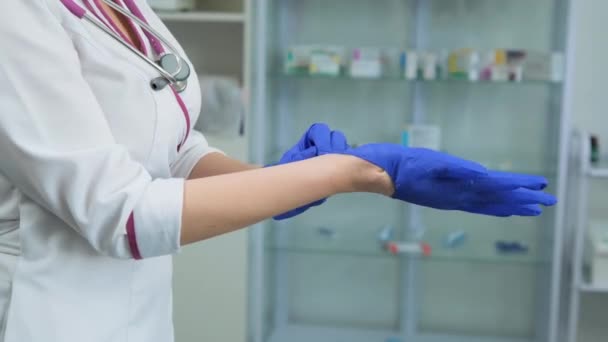 Giovane dottoressa caucasica in mantello medico bianco e stetoscopio viola che indossa guanti blu gomma sulla mano destra in laboratorio o in ospedale. Vista laterale — Video Stock