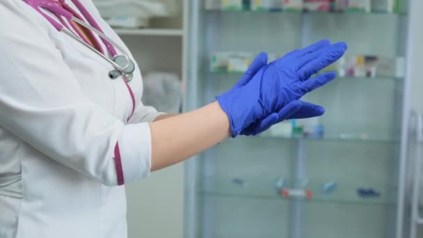 Jonge blanke verpleegster in witte medische jas en violette stethoscoop kijken en controleer een rubber blauwe handschoenen om als het lekkende en kan worden gebruikt. Zijaanzicht — Stockvideo