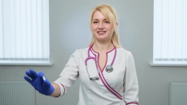 Giovane scienziata caucasica attraente medico in camice medico bianco, stetoscopio viola con una pillola bianca con le dita nei guanti blu nel laboratorio di ricerca farmaceutica — Video Stock