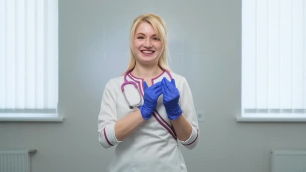 Unga kvinnor läkare håller leksaksfigurer av barn i sina händer nära hjärtat på sjukhus eller klinik på en vit bakgrund. Framifrån. Skydd av barn, kärlek och omsorg. — Stockvideo