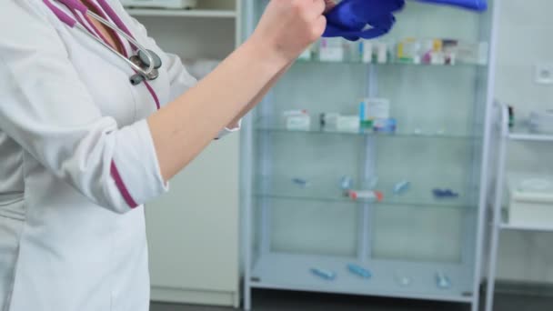 Giovani donne medico caucasico in cappotto medico bianco e stetoscopio viola gonfia un guanto di gomma blu per verificare se è permeabile e può essere utilizzato — Video Stock