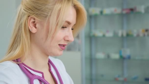 Foto ravvicinata della giovane dottoressa caucasica in camice bianco. Medico donna che lavora al computer portatile e considerando i sintomi della malattia, e scrive una prescrizione sulla rivista medica — Video Stock