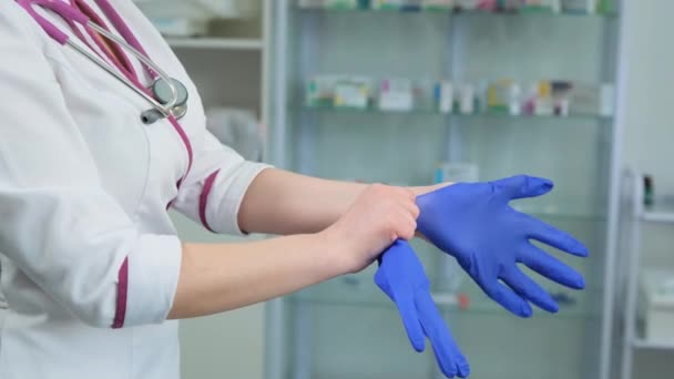 Unga kvinnor läkare läkare i vit kostym klänning och violett stetoskop sätta på gummi blå handskar på vänster hand på sjukhus eller klinik. Sidovy — Stockvideo