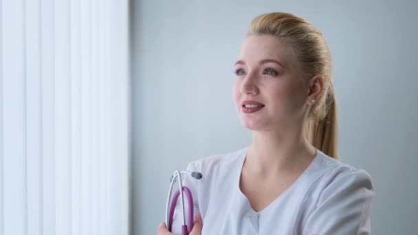 Medic porte un manteau médical tenant un stéthoscope tourne la tête vers la caméra — Video