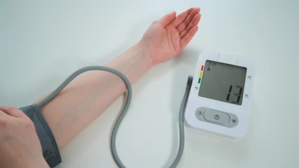 La mujer mide su presión arterial en la mesa. Moderno tonómetro automático blanco y gris que muestra en el monitor los números de medición — Vídeo de stock