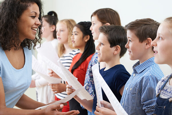 Children In School Choir Being Encouraged By Teacher