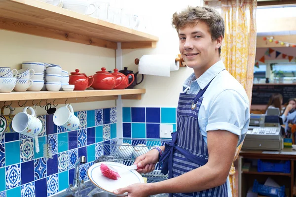 Teenage Boy With Part Time Job Washing Up In Coffee Shop