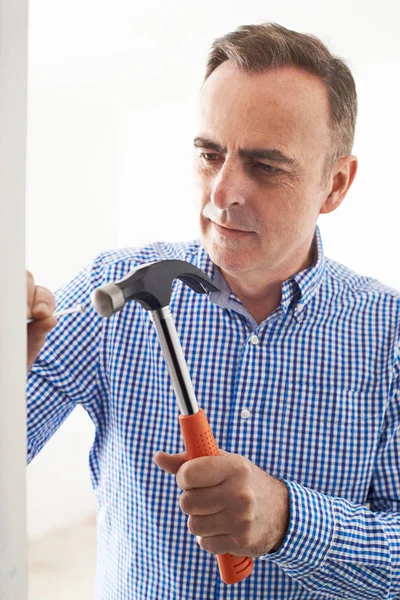 Älterer Mann schlägt Nagel mit Hammer in Wand — Stockfoto