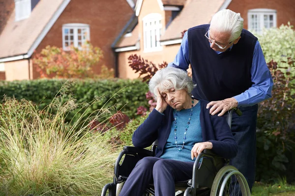 Deprimerade äldre kvinna i rullstol skjuts av man — Stockfoto