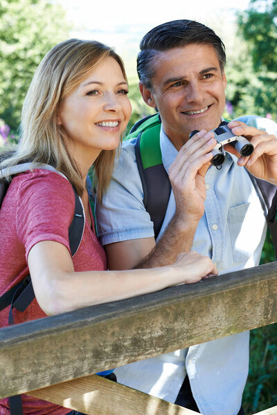 Mature Couple Hiking In Countryside Looking Through Binoculars