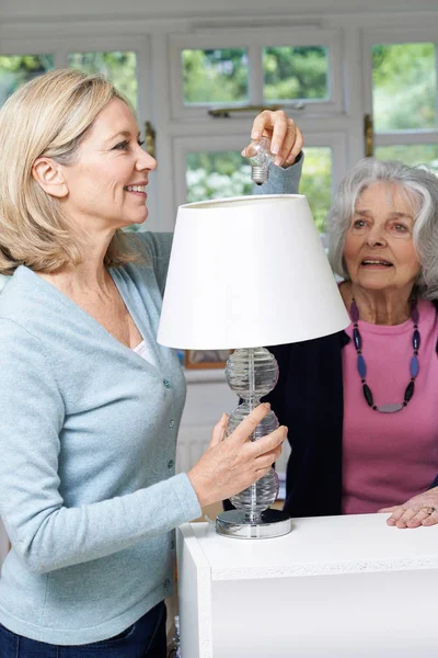 Mujer vecina ayudando a la mujer mayor a cambiar la bombilla en la lámpara — Foto de Stock