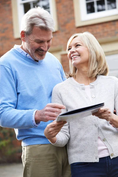 Älteres Ehepaar steht vor Haus und schaut sich Immobiliendetails an — Stockfoto