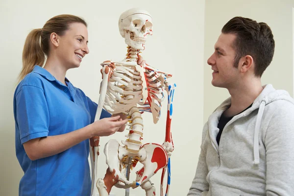 Osteópata discutiendo lesión con paciente usando esqueleto — Foto de Stock