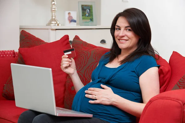 Gravid kvinna som sitter på soffan med kreditkort att handla Online — Stockfoto