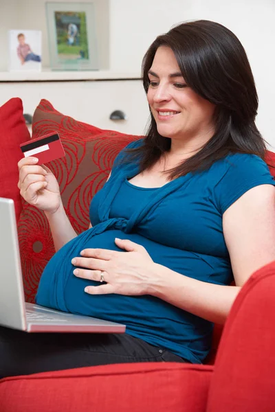 Femme enceinte assise sur le canapé en utilisant une carte de crédit pour acheter en ligne — Photo