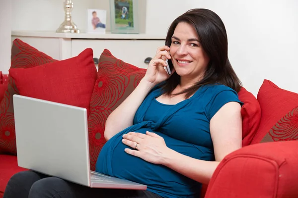 Zwangere vrouw zittend op de Bank met behulp van Laptop en mobiele telefoon — Stockfoto