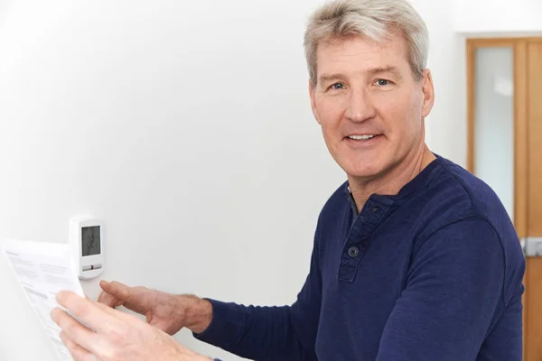 Smiling Mature Man With Bill Adjusting Central Heating Thermosta — Stock Photo, Image