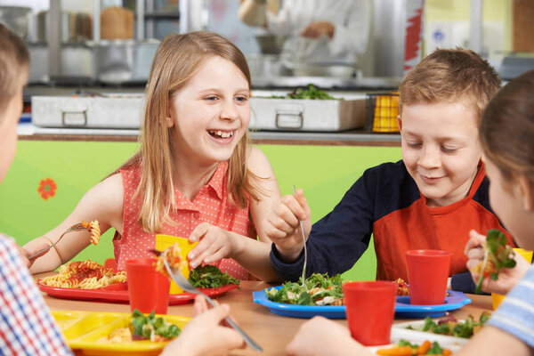 Group Of Pupils Sitting At Table In School Cafeteria Eating Lunc