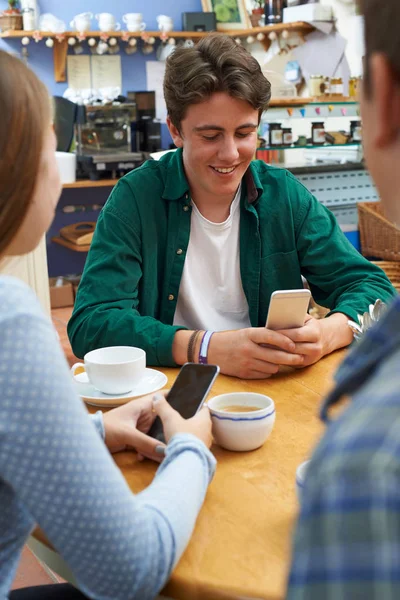 Встреча группы друзей-подростков в кафе и использование мобильных телефонов — стоковое фото