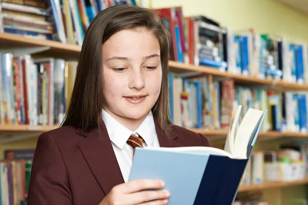 Flicka klädd skola enhetlig läsebok i biblioteket — Stockfoto