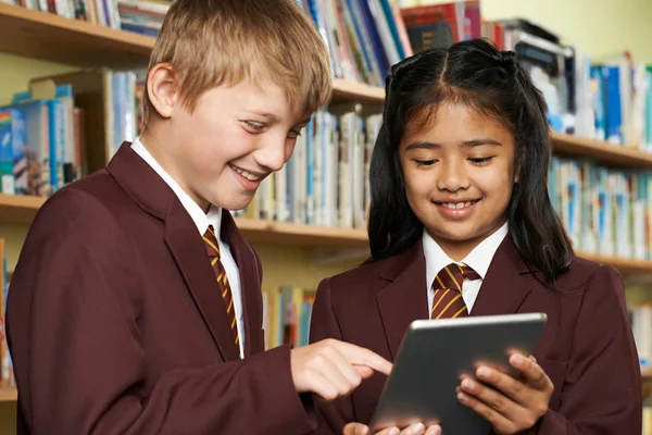Alumnos vistiendo uniforme escolar usando tableta digital en la biblioteca —  Fotos de Stock