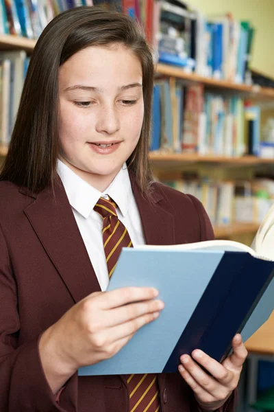 Flicka klädd skola enhetlig läsebok i biblioteket — Stockfoto