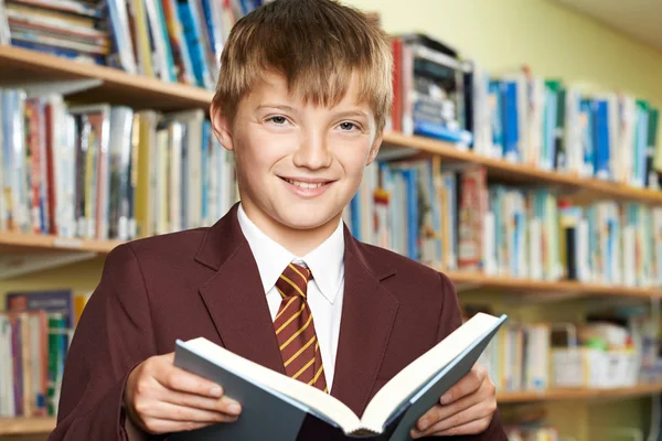 Junge in Schuluniform liest Buch in Bibliothek — Stockfoto