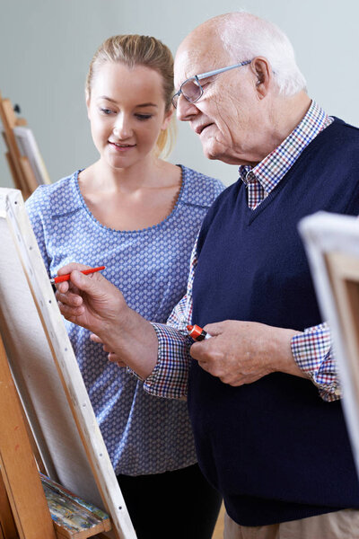 Senior Man Attending Painting Class With Teacher
