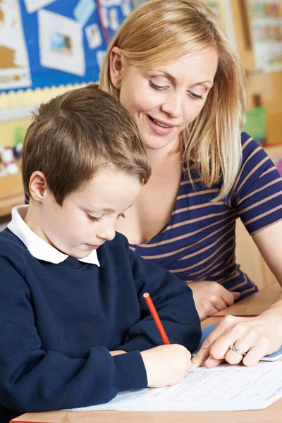 Lehrerin hilft männlichem Grundschüler bei Schreibtischarbeit — Stockfoto